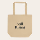 Beige tote bag with 'Still Rising' text on a white background