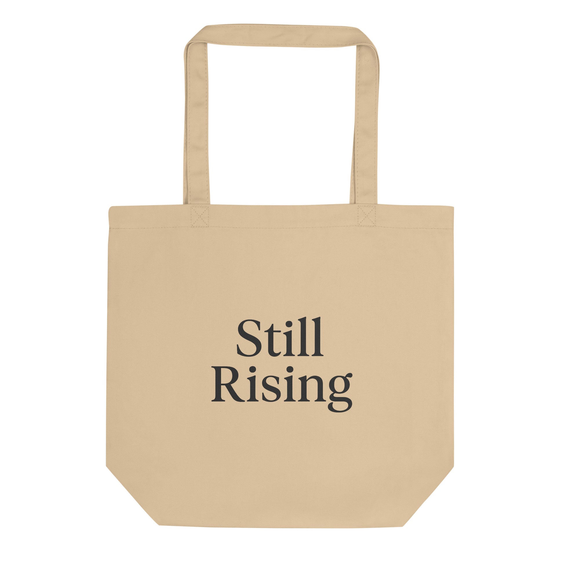 Beige tote bag with 'Still Rising' text on a white background