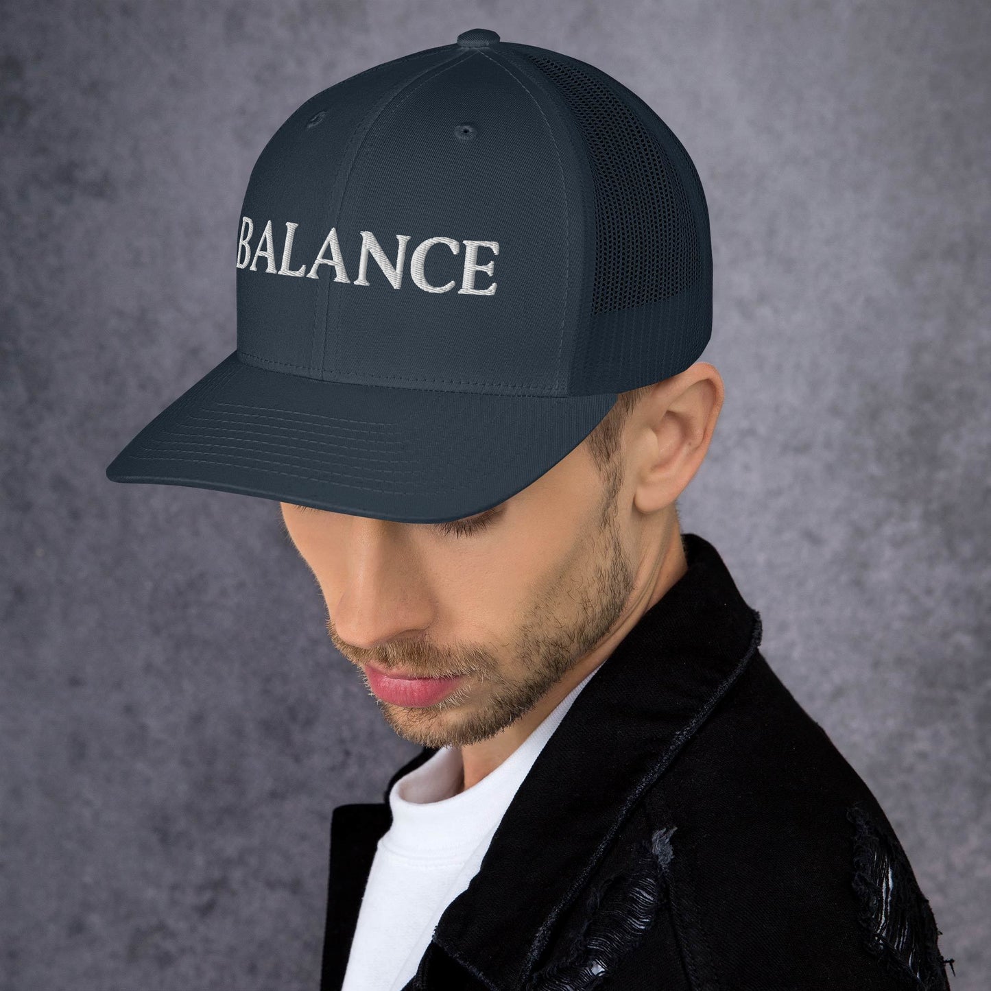 Man wearing a black cap with 'BALANCE' embroidered on it against a gray background