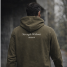 Person wearing a green hoodie with 'Strength Without Armor' text in a forest setting