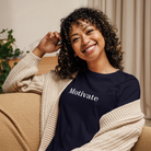 Woman wearing a black sweatshirt with 'Motivate' text, sitting on a couch.